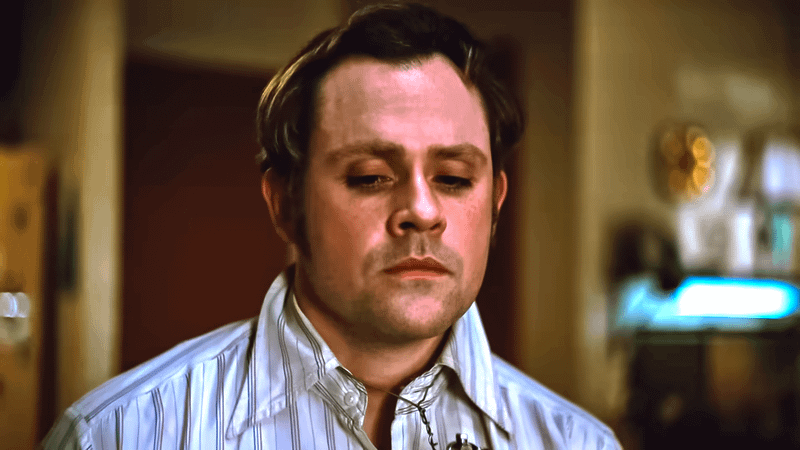 Dacre Montgomery as Richard Hall in a striped button-up looking downward in Head Man's Wire