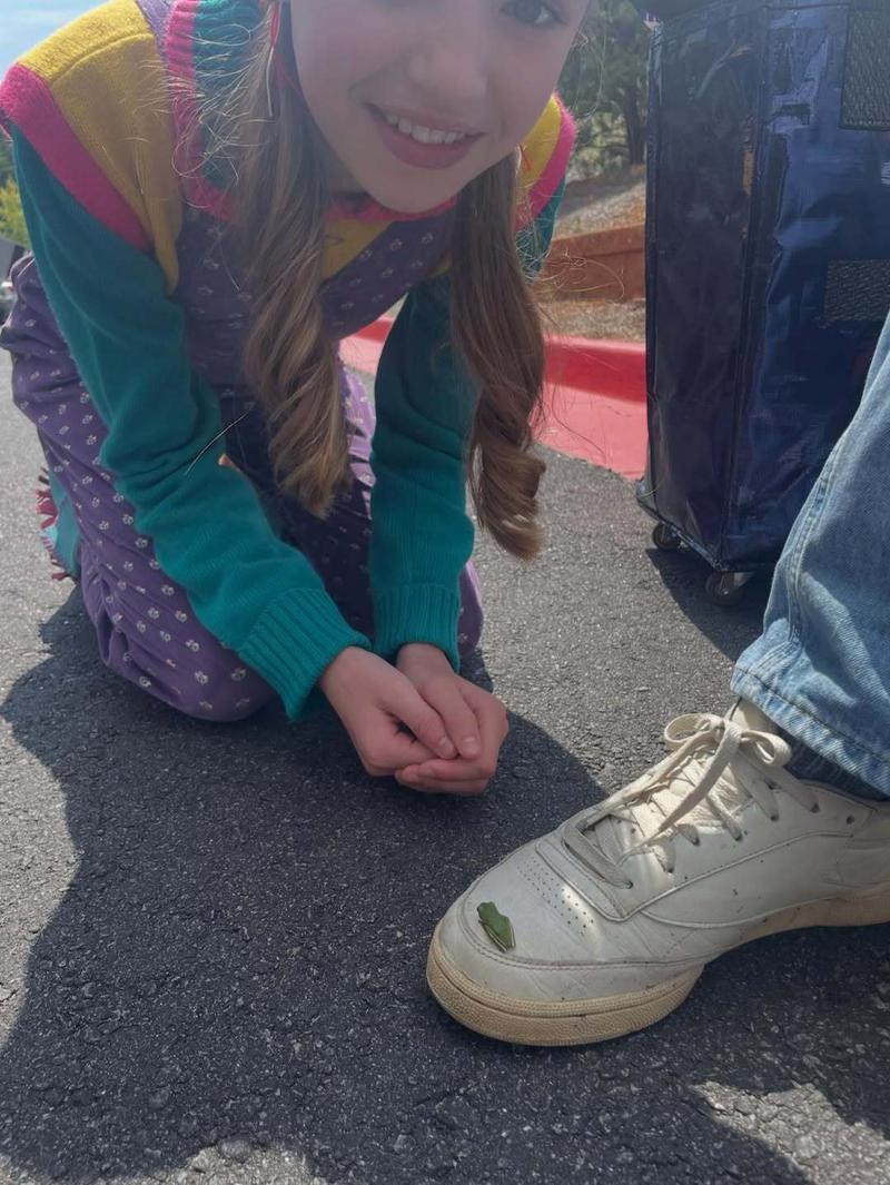 Nell Fisher leaning down and looking at a small frog on a shoe on the set of Stranger Things