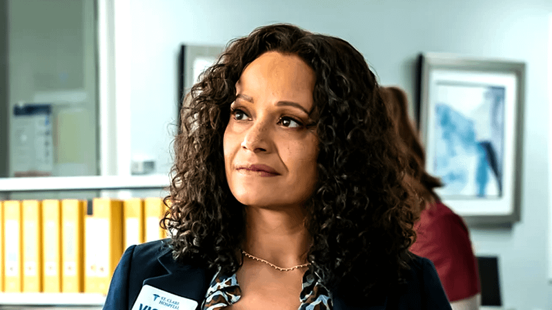 Judy Reyes as Carla Espinosa standing in a hospital lobby in a blazer in Scrubs.
