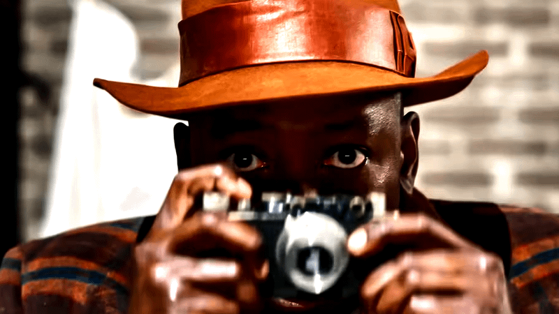 Lamorne Morris as Robbie Robertson holding a camera in Spider-Noir.