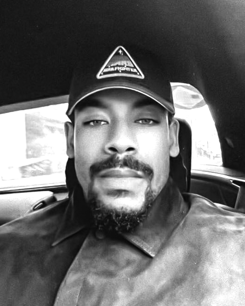 Aaron Pierre wears a baseball cap featuring the Star Wars: Starfighter logo in a black-and-white photo.