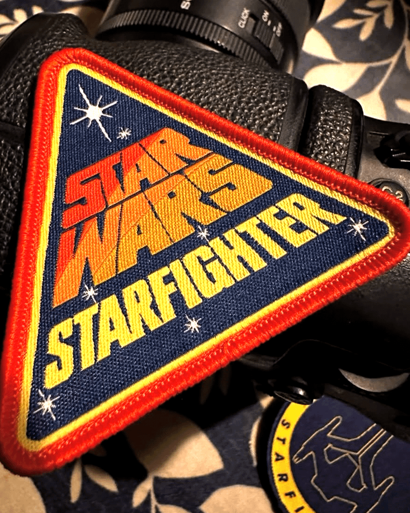 A color image of the Star Wars: Starfighter logo on a triangular patch sitting atop a professional camera.