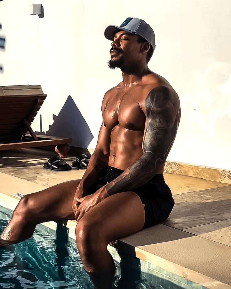 Aaron Pierre sitting by a pool in swim trunks.