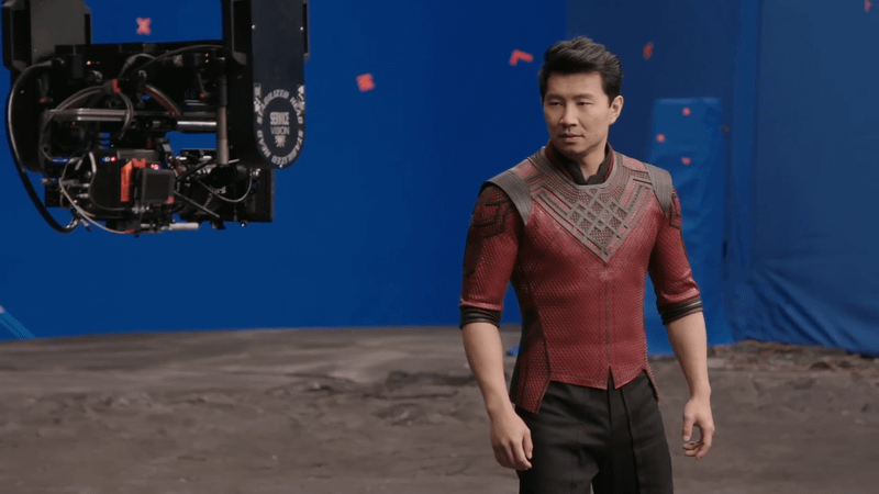 Simu Liu wears his red and black Shang-Chi suit in front of a blue screen as a camera captures his performance in a Marvel Studios: Assembled episode about Shang-Chi and the Legend of the Ten Rings.
