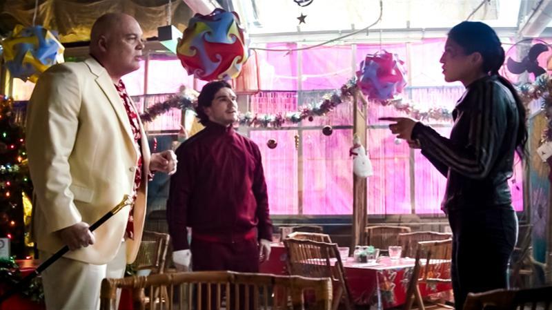 Wilson Fisk, Kazi and Maya Lopez talking in a brightly decorated room with several windows. Maya points at Fisk, who stands next to Kazi. They are surrounded by tables and chairs.